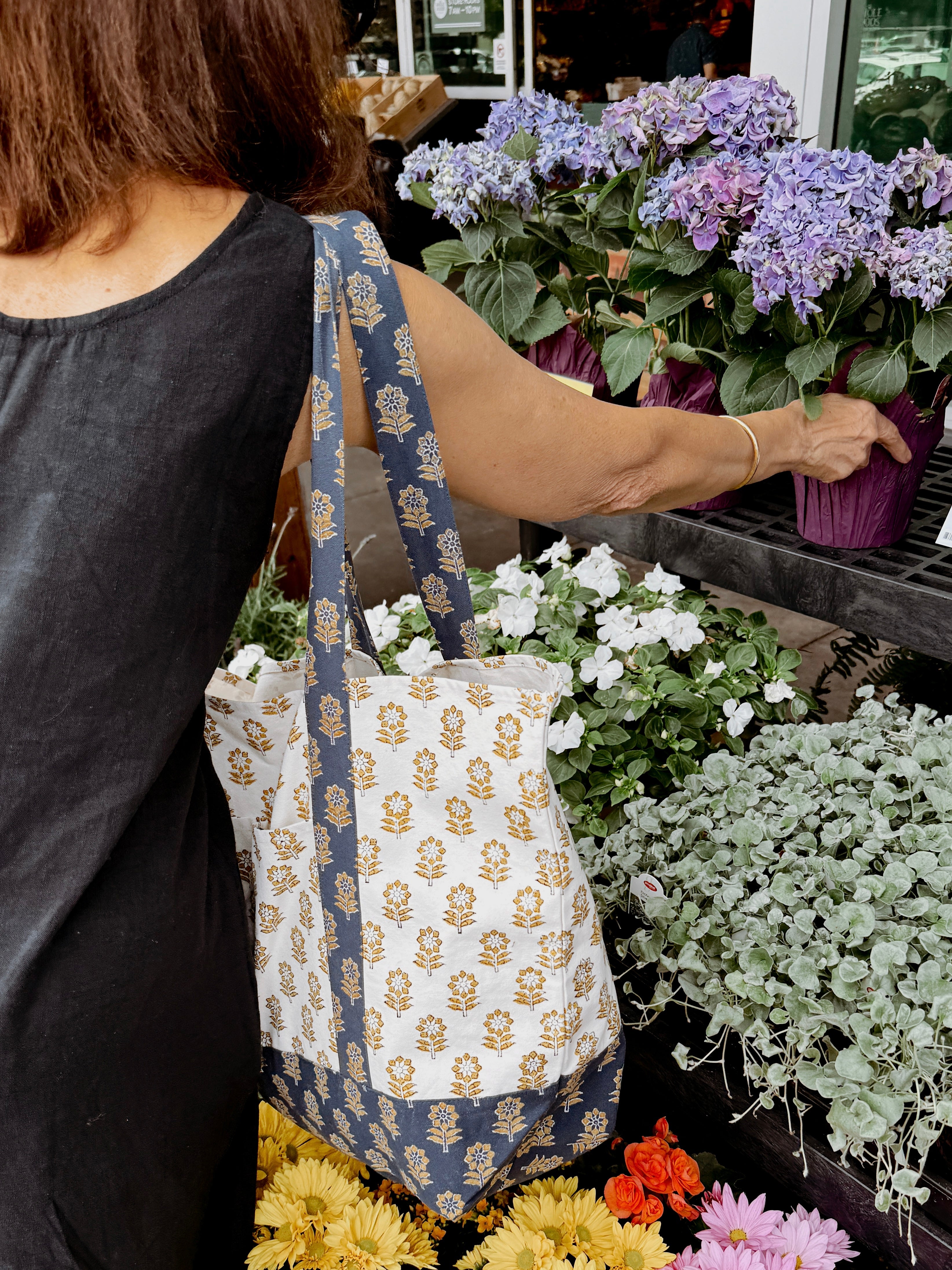 Woman wearing blue and gold floral printed tote bag while picking out flowers