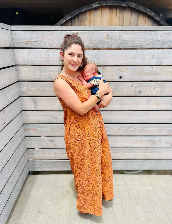 Woman wearing orange sleeveless jumpsuit and holding baby