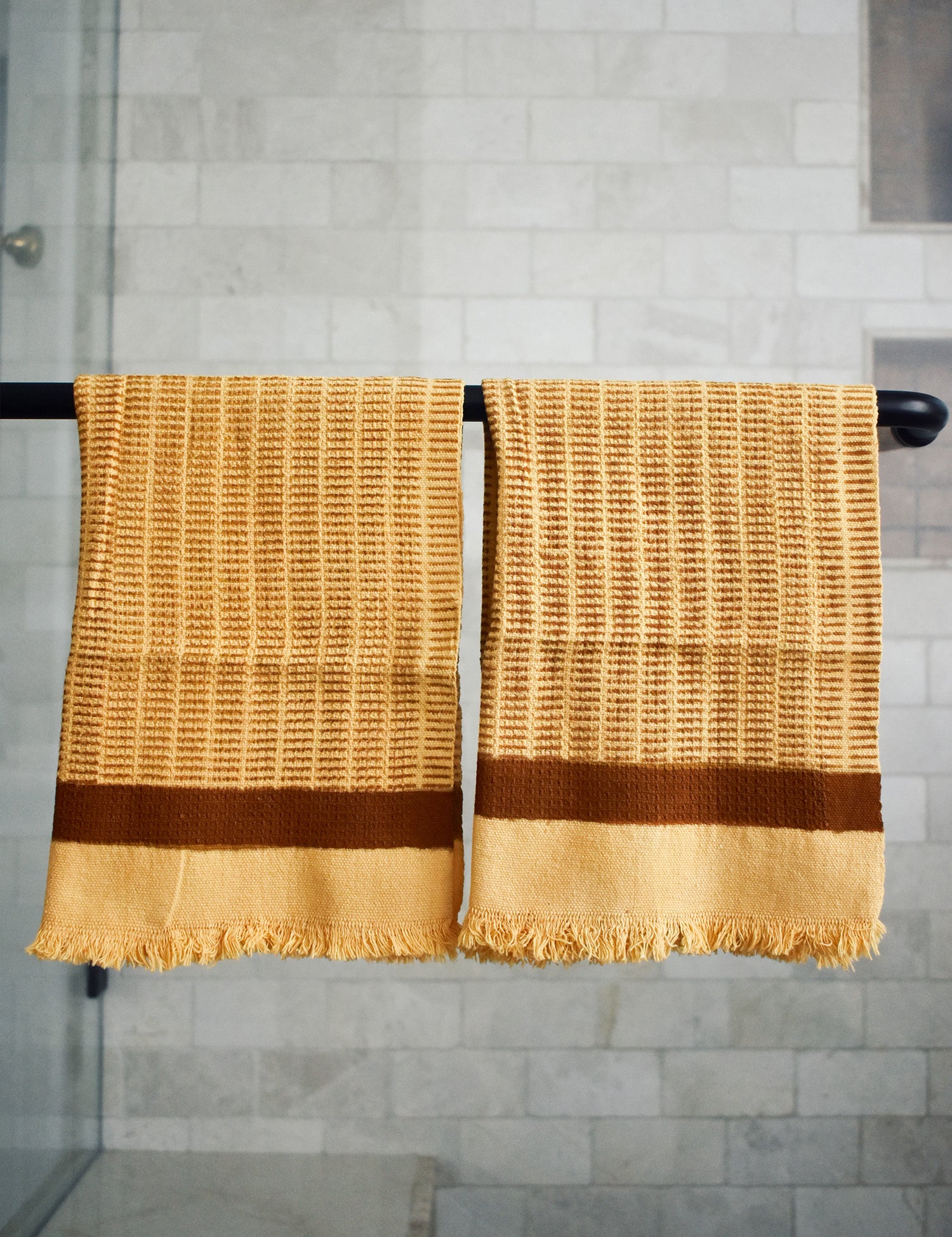 Block printed Feliz hand towels hanging on a black rod outside a shower