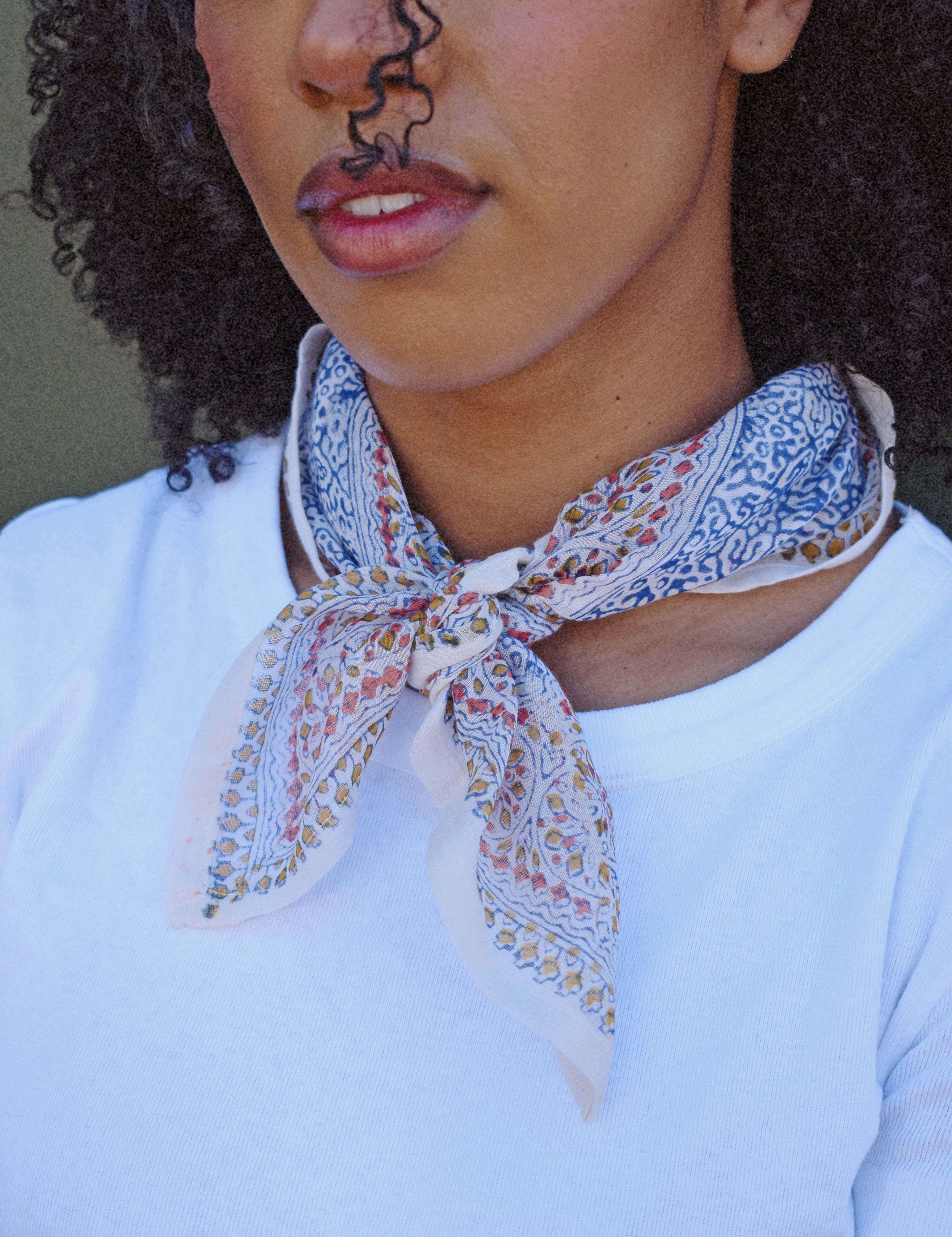 Woman wearing a floral patterned scarf around their neck against a white tee with a green background