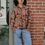 Person wearing a floral patterned corduroy shirt and jeans standing against a brick wall.