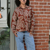 Person wearing a floral patterned corduroy shirt and jeans standing against a brick wall.
