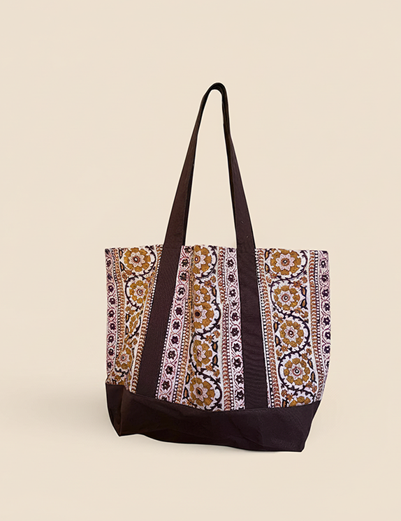 Brown and gold floral printed tote bag standing up against creamish yellow background