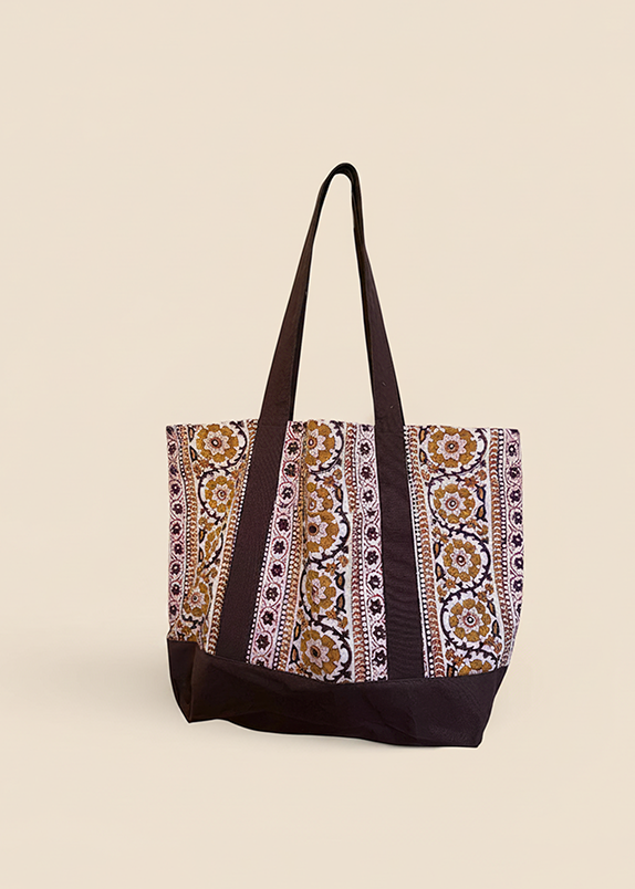 Brown and gold floral printed tote bag standing up against creamish yellow background