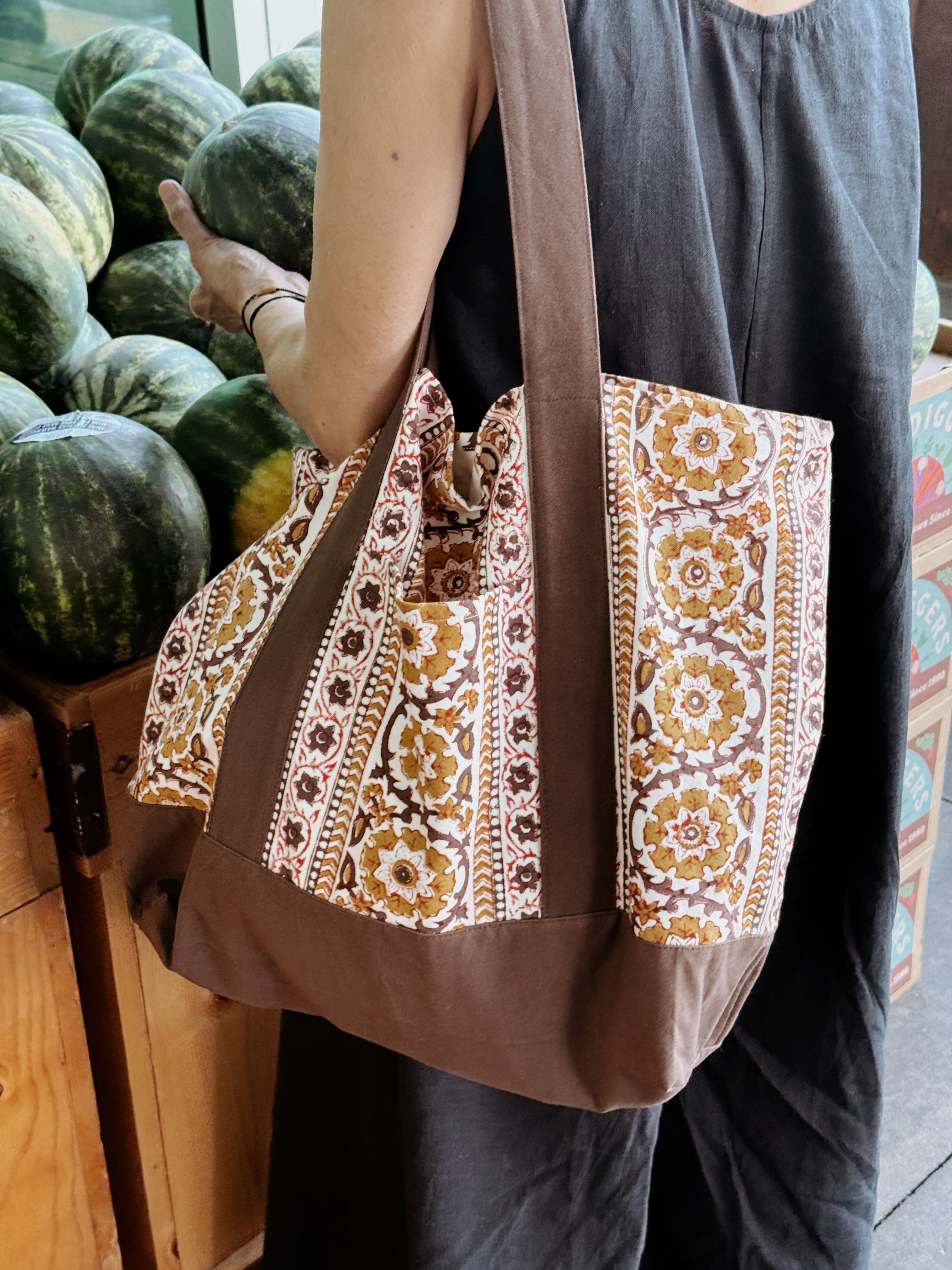 Woman wearing brown and gold floral printed tote bag while shopping for melons
