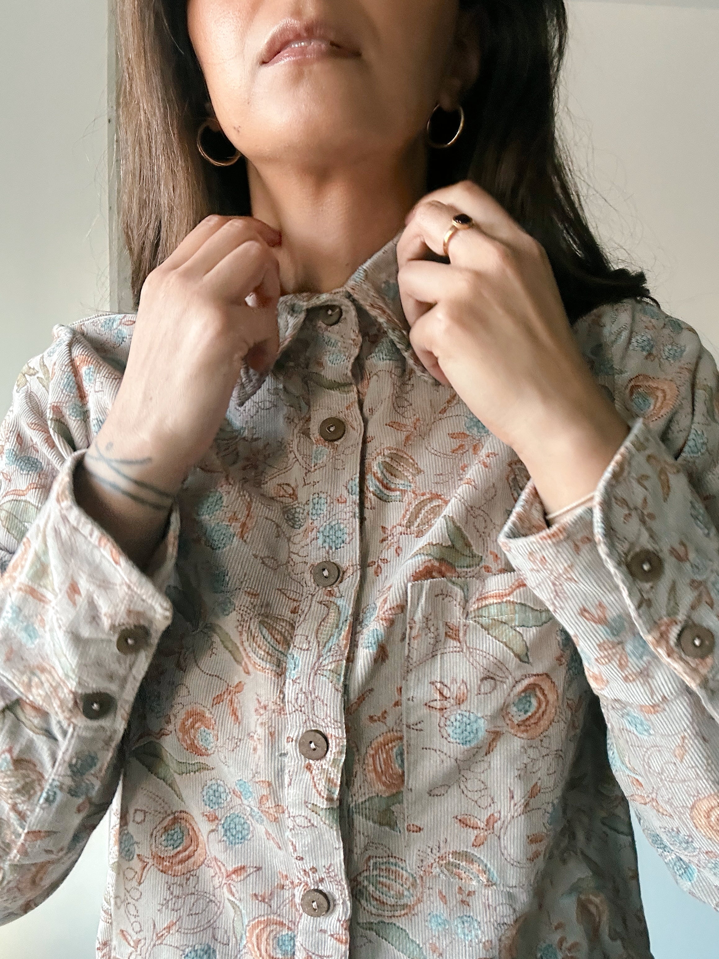 Woman buttoning up Helena corduroy floral printed shirt, close up on buttons
