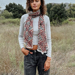 Woman wearing block printed Layla georgette scarf around the neck, paired with grey long sleeve and black jeans. Woman is standing outside.