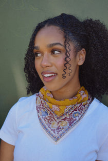 Woman wearing a colorful yellow bandana scarf standing in front of a green background