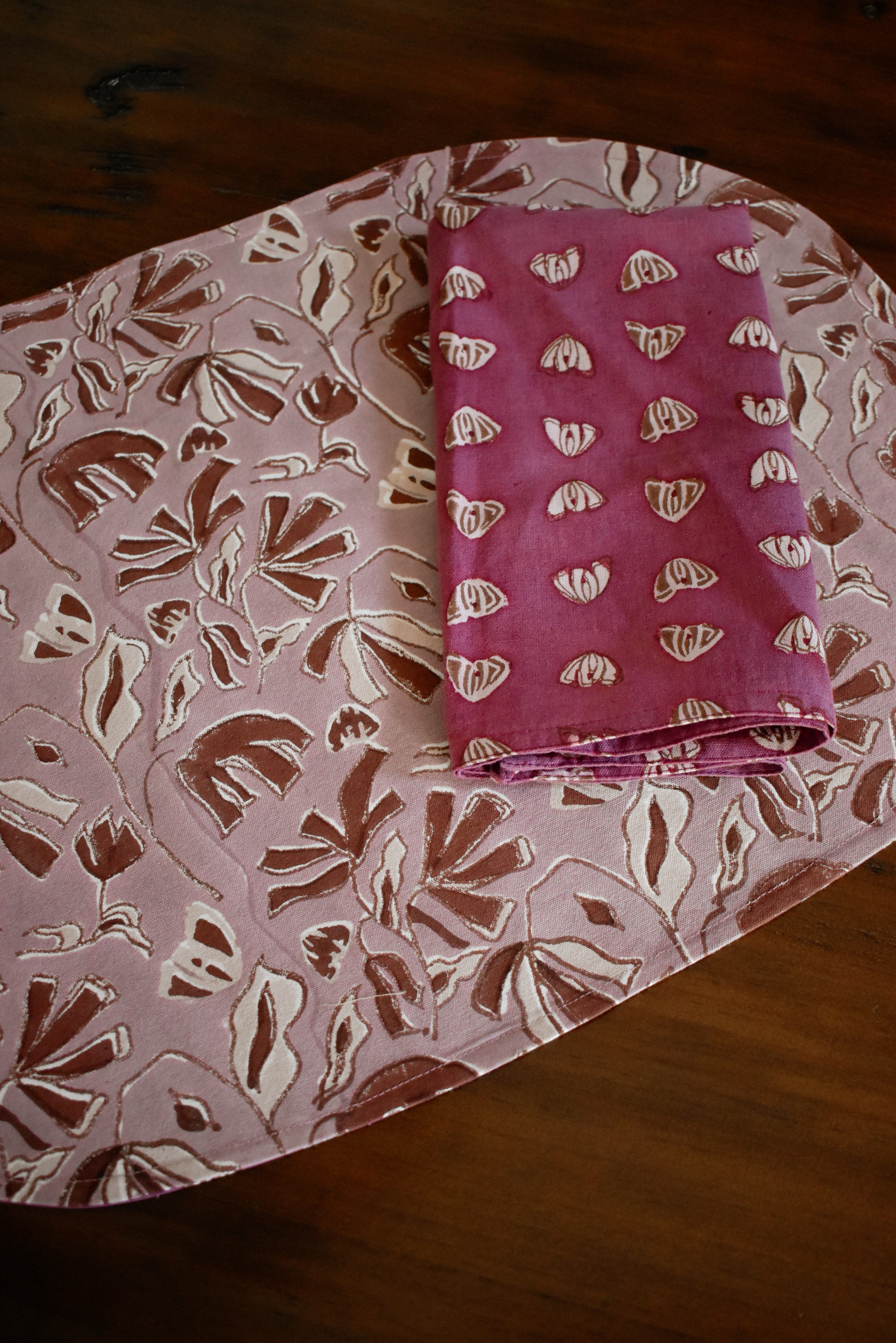 Large floral printed placemat with purple floral printed table napkin on a wooden table