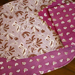 Purple and pink floral printed placemats and table napkins on a wooden table.