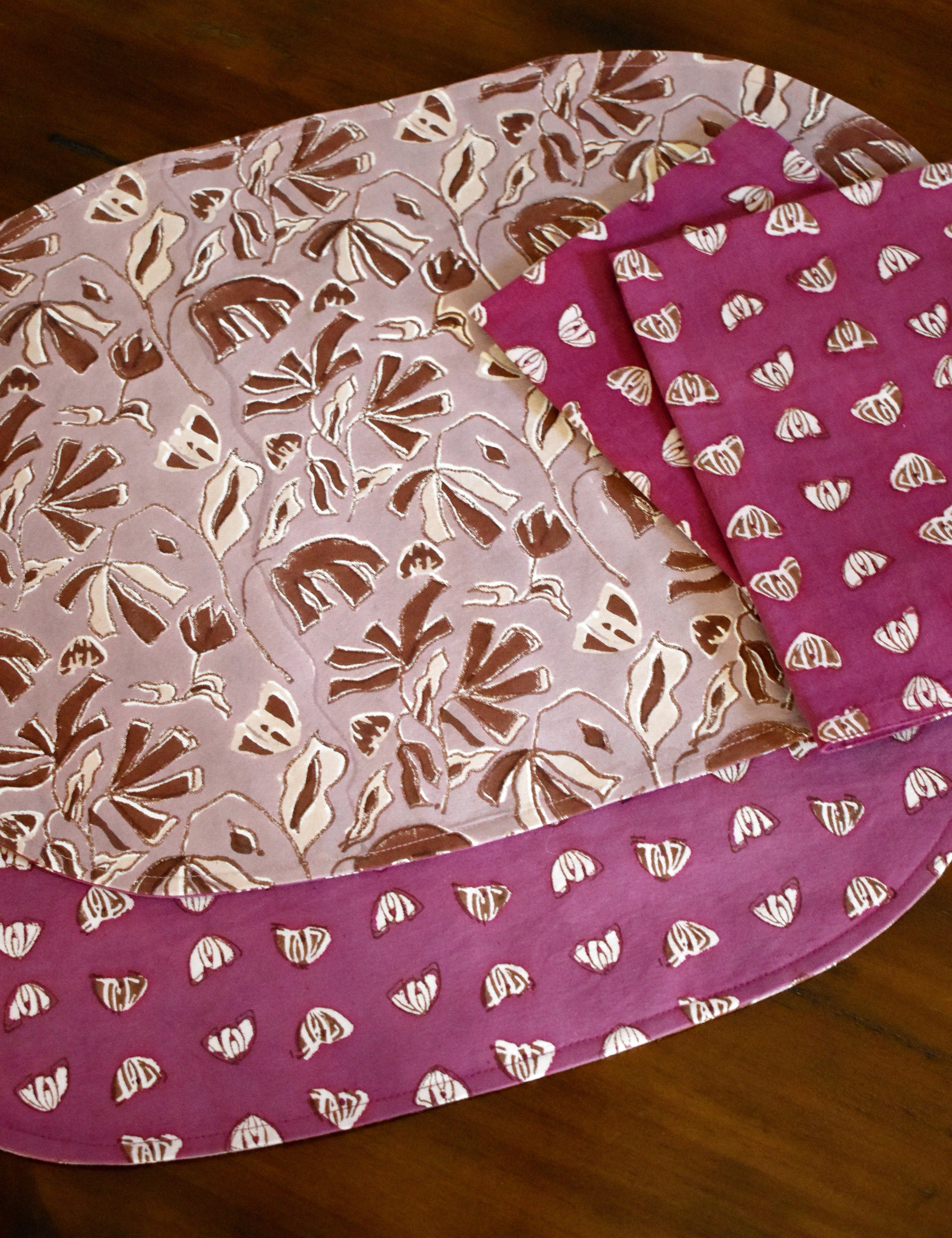 Purple and pink floral printed placemats and table napkins on a wooden table.