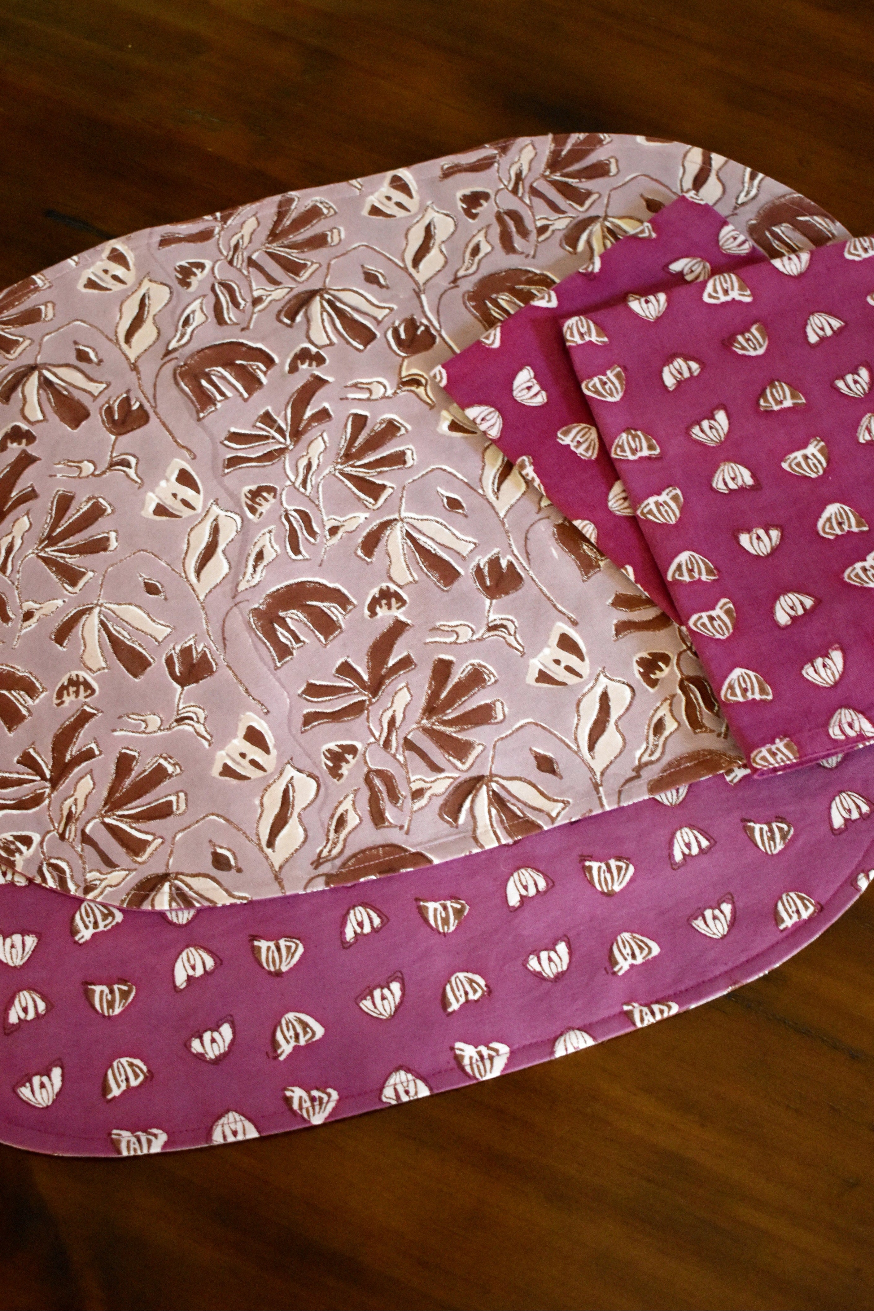 Purple and pink floral printed placemats and table napkins on a wooden table.