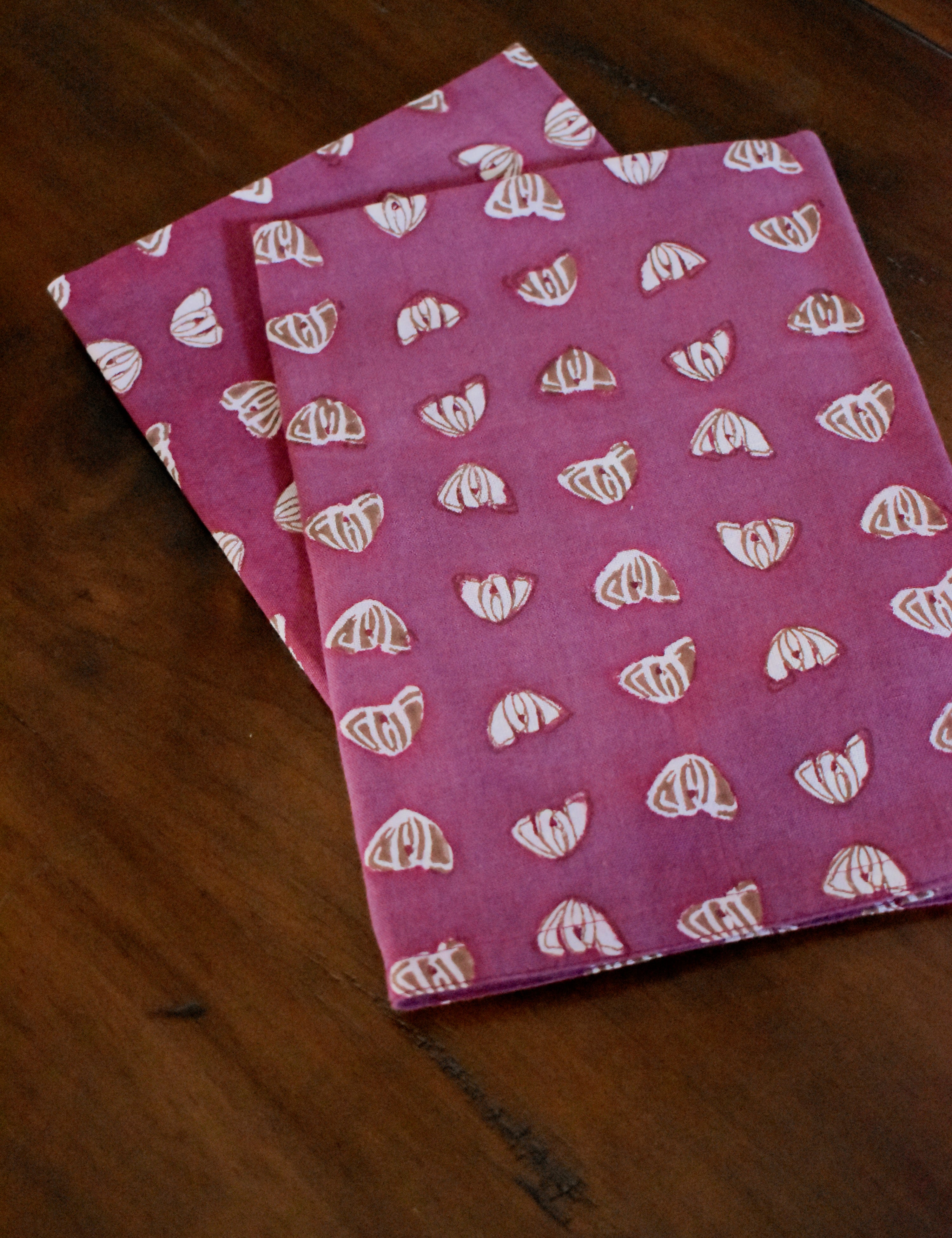 Two purple table napkins with floral print folded on wooden table