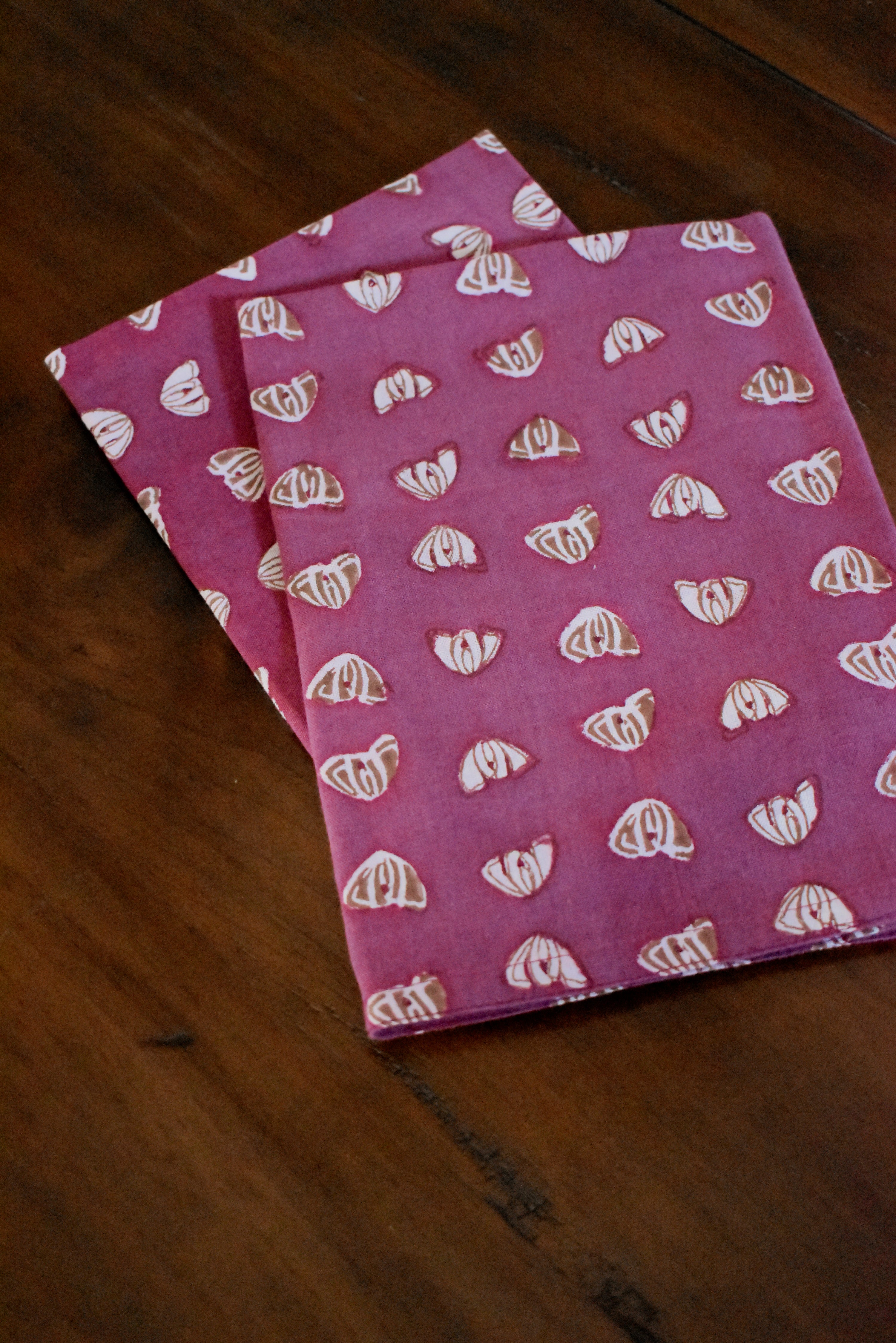 Two purple table napkins with floral print folded on wooden table
