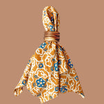 Napkin scrunched up and styled with wooden napkin holder. Napkin has a block printed orange and blue floral print all over