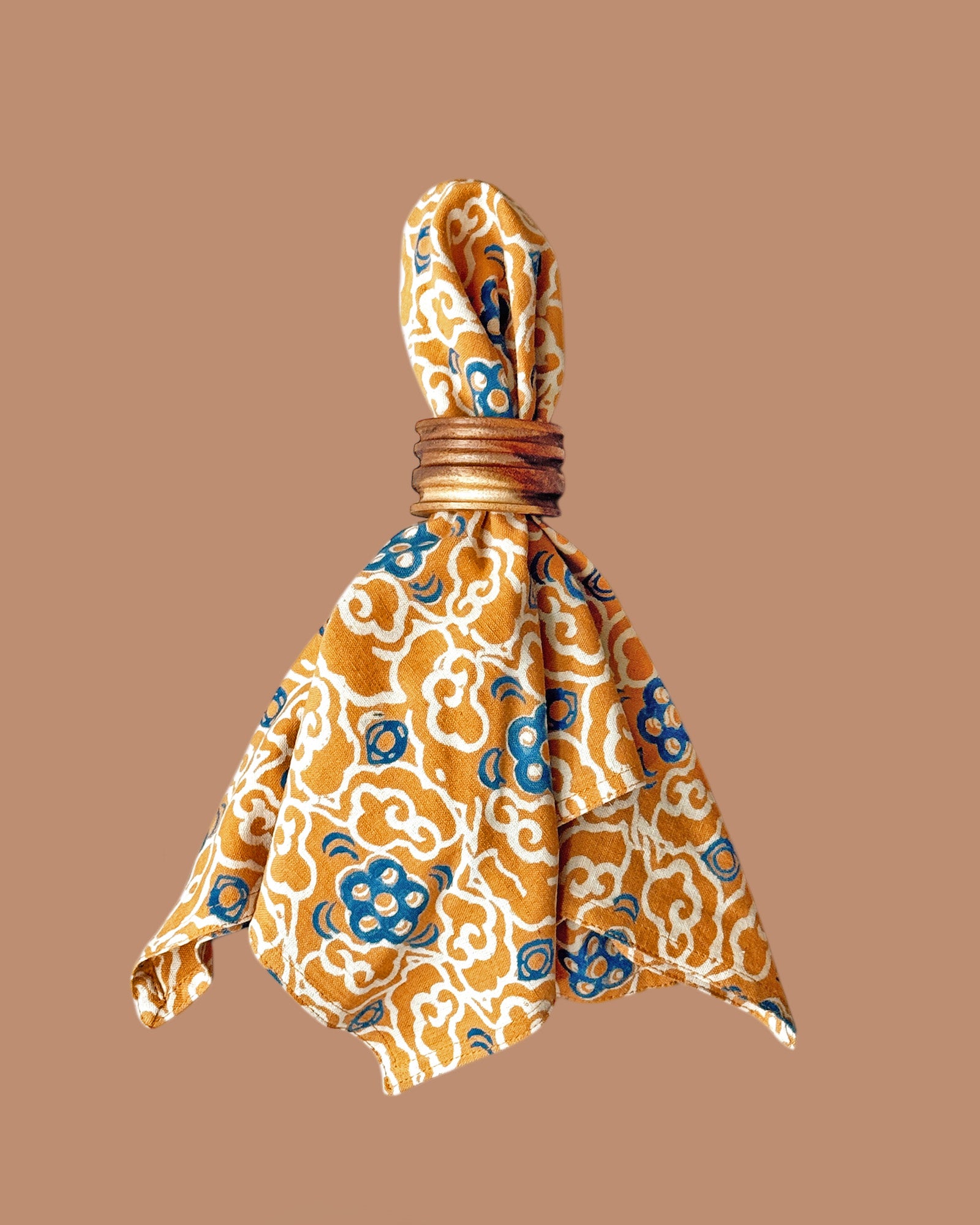 Napkin scrunched up and styled with wooden napkin holder. Napkin has a block printed orange and blue floral print all over