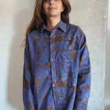 Person wearing a blue and brown floral patterned corduroy shirt against a concrete wall.