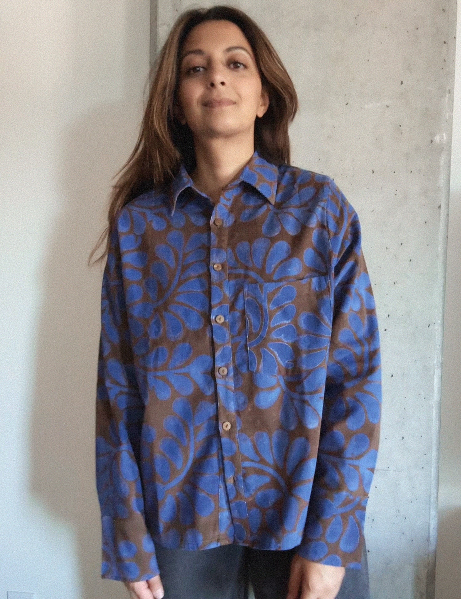 Person wearing a blue and brown floral patterned corduroy shirt against a concrete wall.
