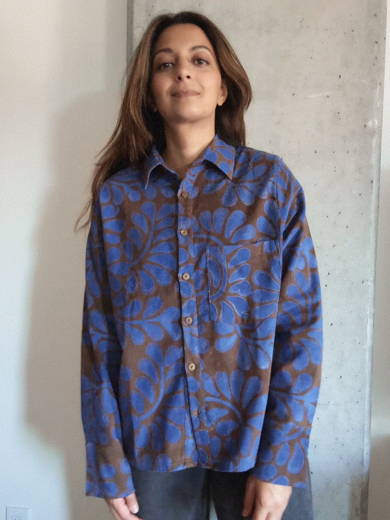 Person wearing a blue and brown floral patterned corduroy shirt against a concrete wall.