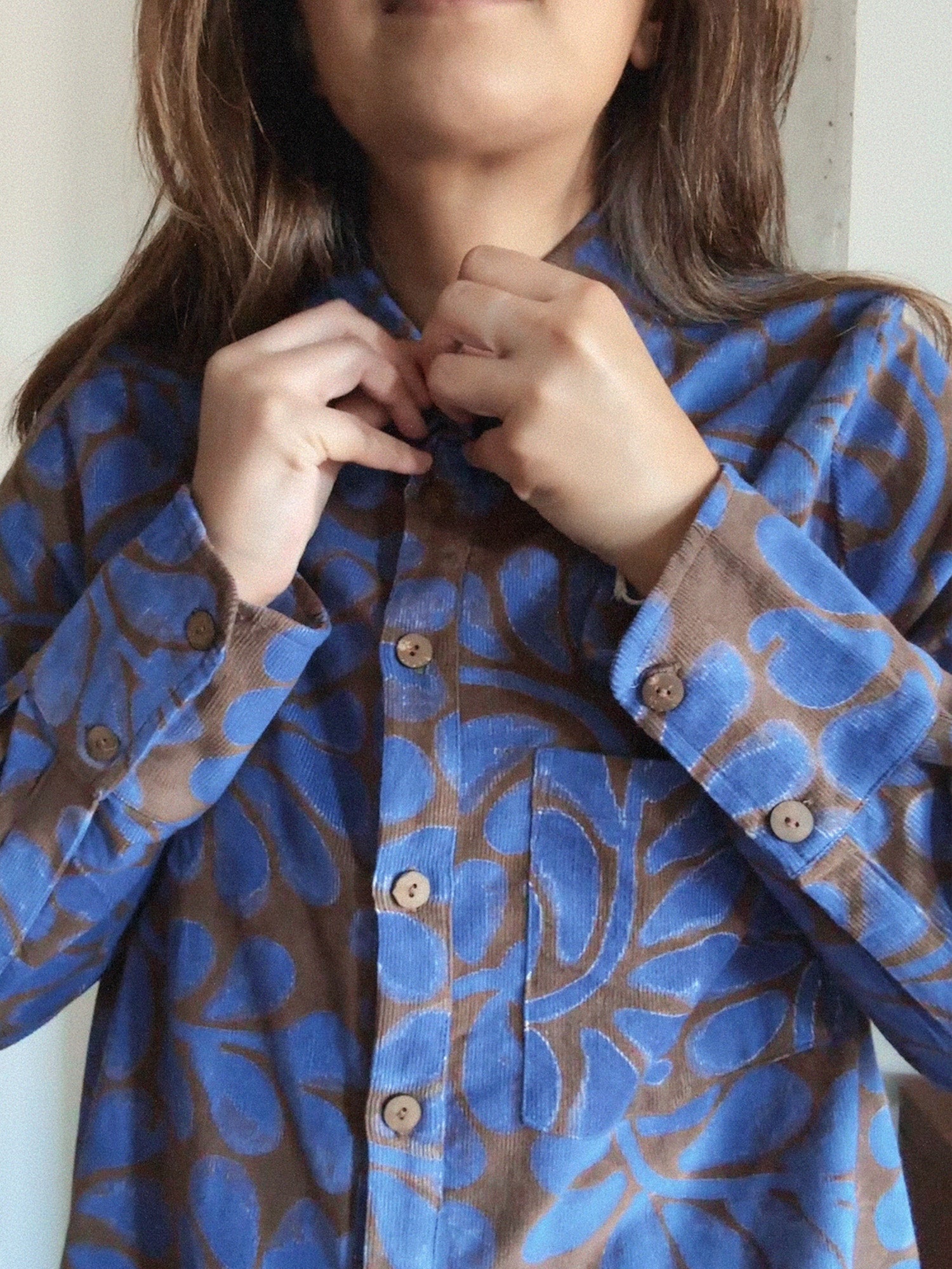 Person wearing a blue and brown patterned shirt with wooden buttons.