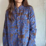 Person wearing a blue and brown floral patterned shirt against a concrete wall.