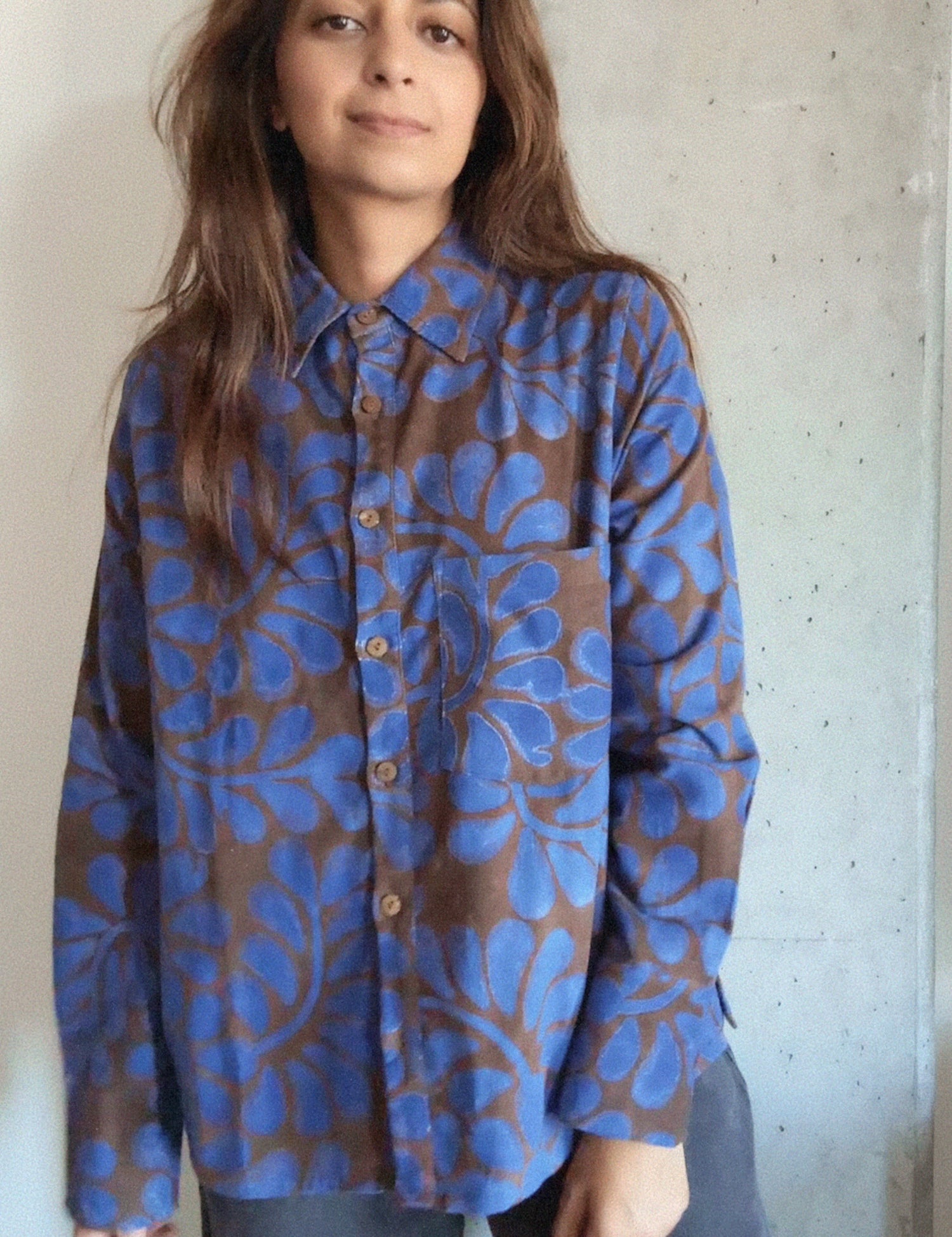 Person wearing a blue and brown floral patterned shirt against a concrete wall.