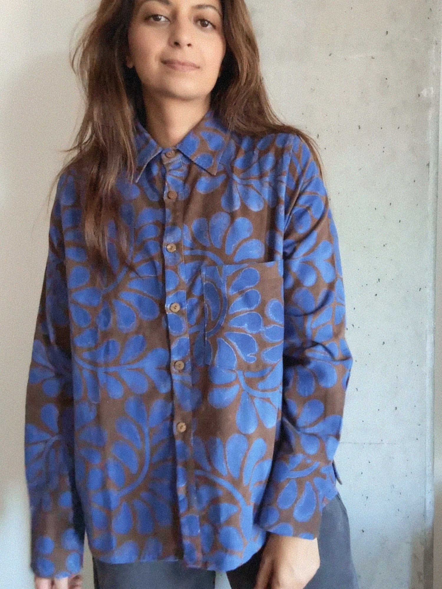 Person wearing a blue and brown floral patterned shirt against a concrete wall.
