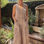 Woman in a black and white floral patterned jumpsuit standing in a garden with plants and a fountain.