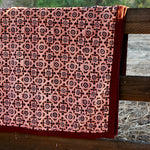 Close up print of the Orchard velvet blanket to show red and pink geometric floral print that is on one side of the blanket. Blanket is draped over a wooden fence in a rustic setting. 
