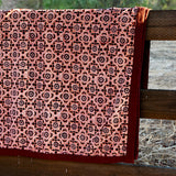 Close up print of the Orchard velvet blanket to show red and pink geometric floral print that is on one side of the blanket. Blanket is draped over a wooden fence in a rustic setting. 