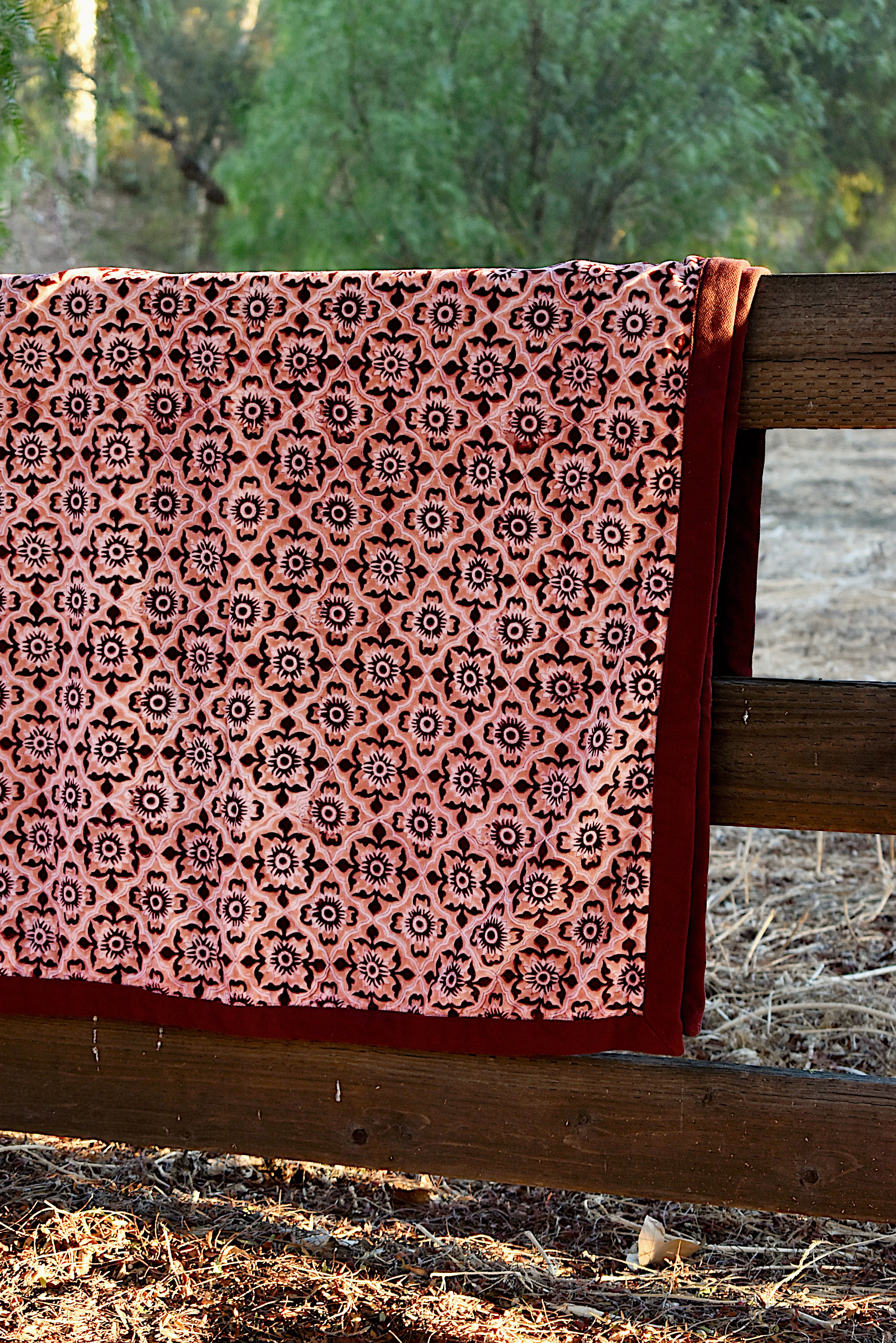 Close up print of the Orchard velvet blanket to show red and pink geometric floral print that is on one side of the blanket. Blanket is draped over a wooden fence in a rustic setting. 