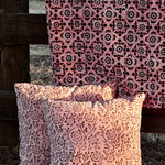 Floral printed blanket draped over a wooden fence in a rustic setting. Two pillows with different floral print sitting on ground in front of the blanket.
