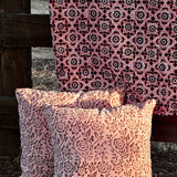 Floral printed blanket draped over a wooden fence in a rustic setting. Two pillows with different floral print sitting on ground in front of the blanket.