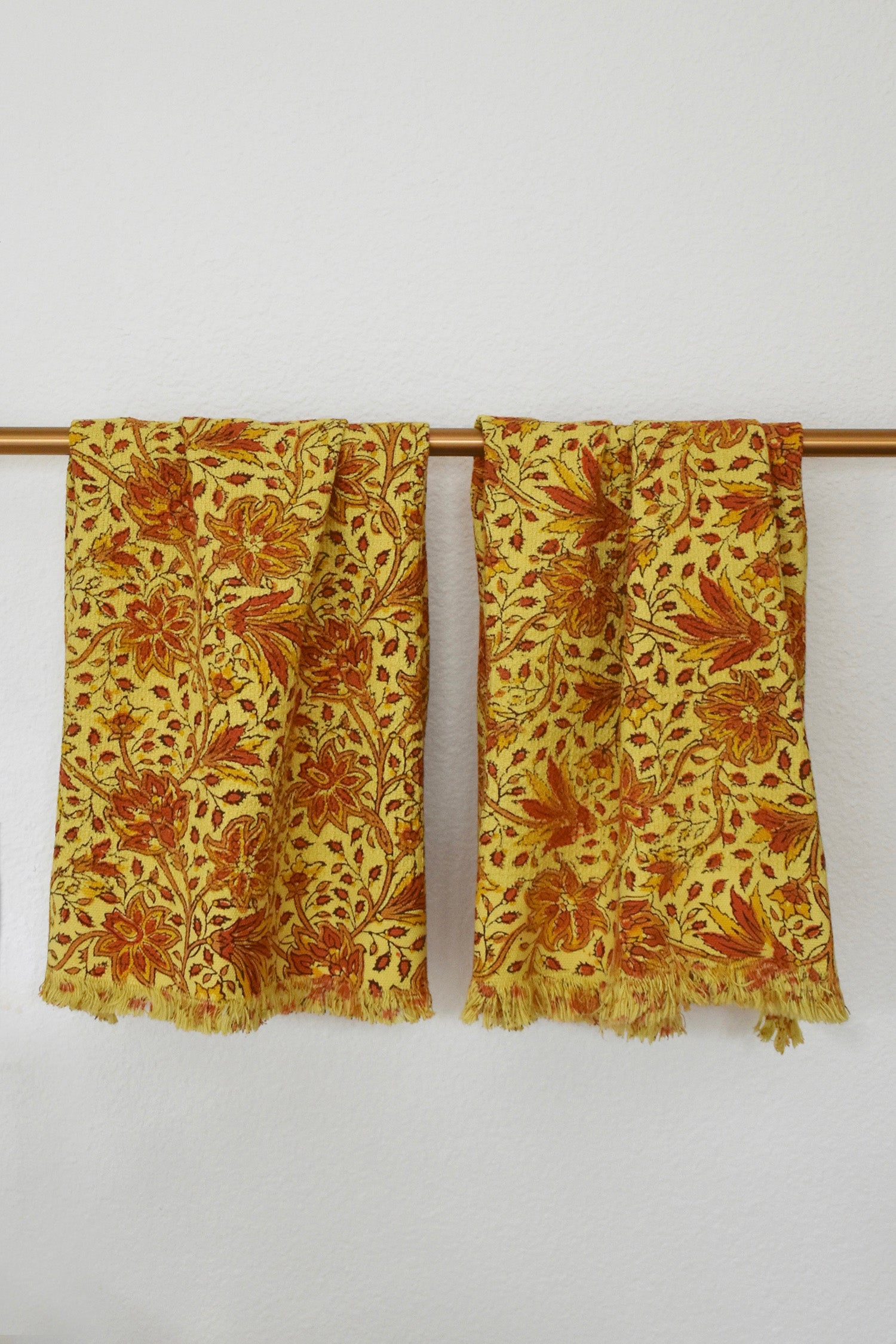 Two Penelope block printed khadi cotton hand towels hanging on a gold bathroom rod