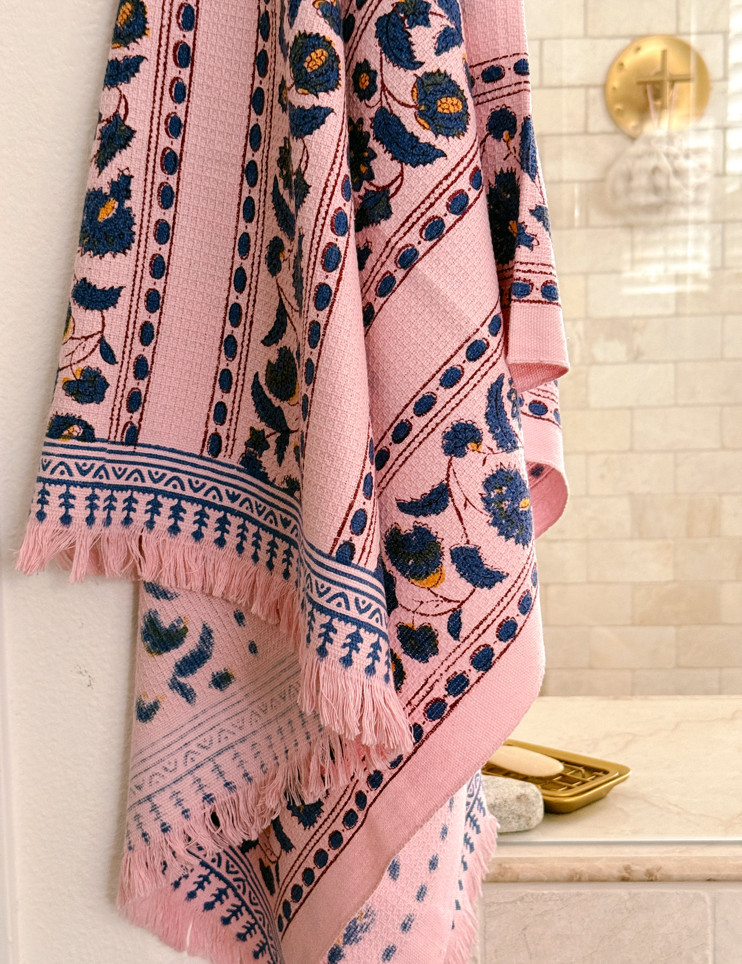 A pink bath towel with navy floral and geometric patterns, hanging in front of a shower