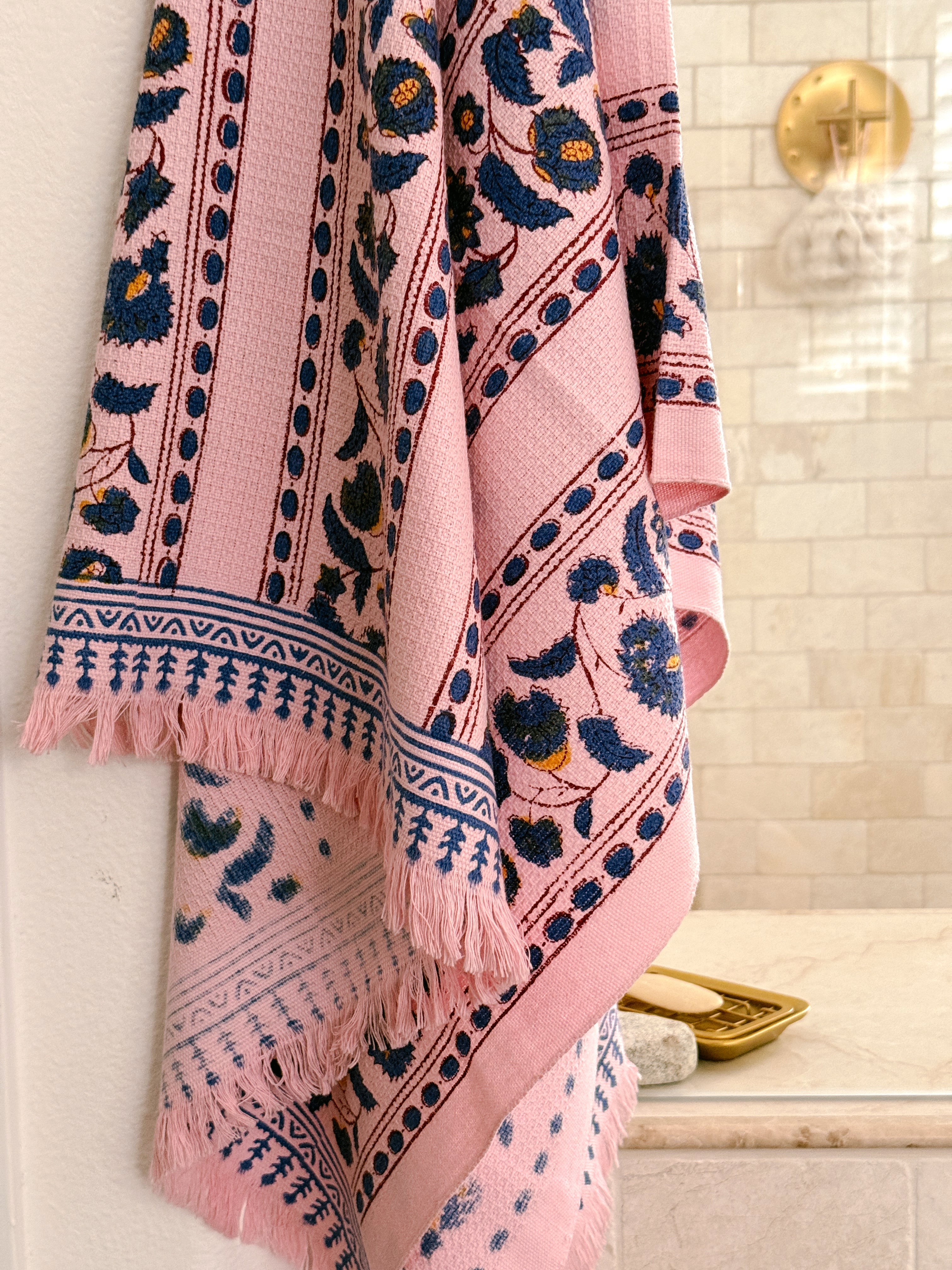 A pink bath towel with navy floral and geometric patterns, hanging in front of a shower