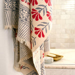 A beige woven towel with red and gray botanical and geometric patterns hung in front of a tiled shower