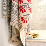 A beige woven towel with red and gray botanical and geometric patterns hung in front of a tiled shower