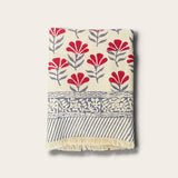 A folded woven bath towel with a cream base, featuring red floral motifs, gray leafy stems, a decorative gray border, and gray diagonal stripes with cream fringe, shown on a light beige background.