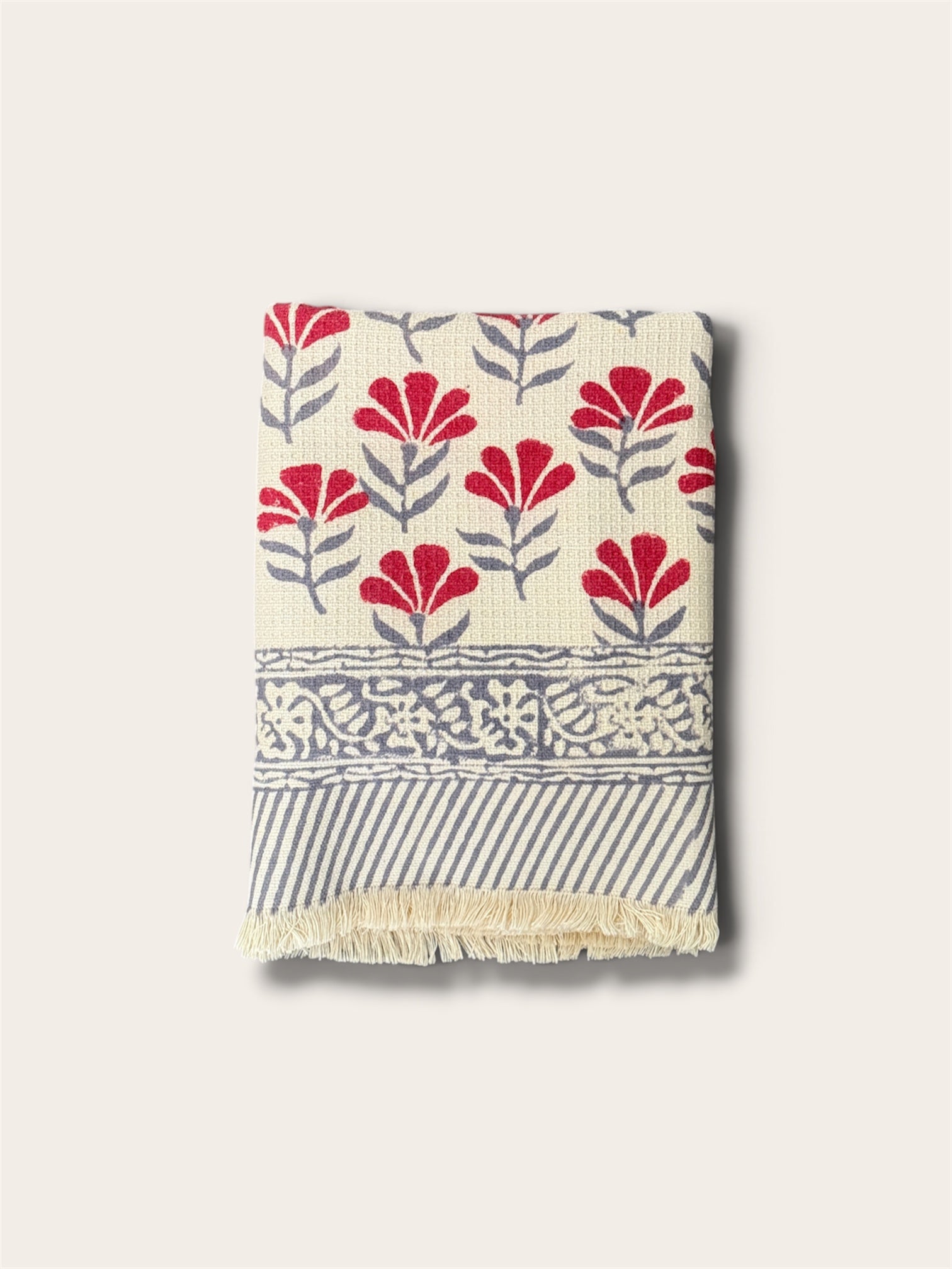 A folded woven bath towel with a cream base, featuring red floral motifs, gray leafy stems, a decorative gray border, and gray diagonal stripes with cream fringe, shown on a light beige background.