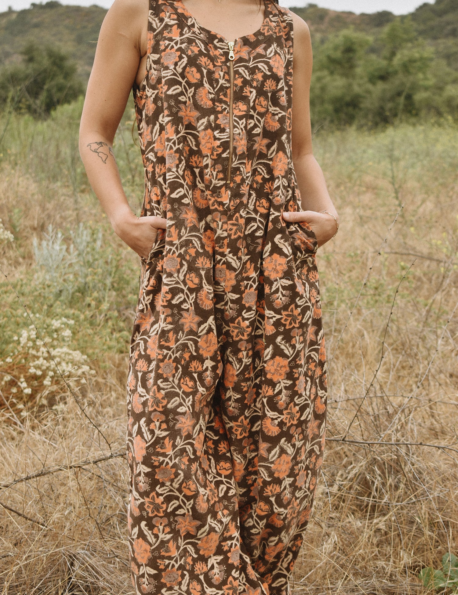 Close up of block printed floral printed Regina Corduroy Jumpsuit, hands in pockets, woman standing in a field