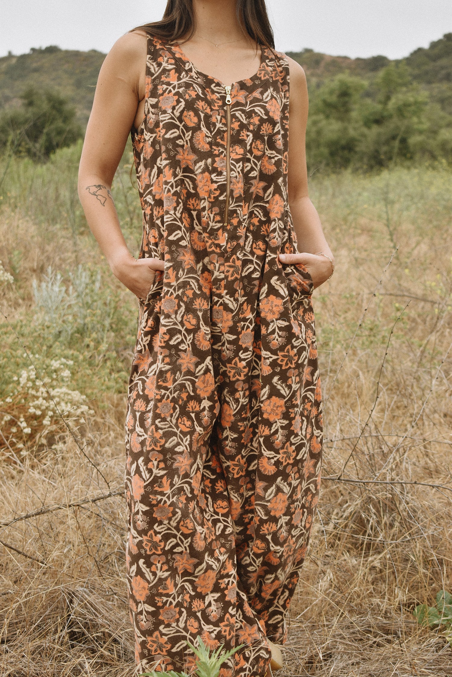 Close up of block printed floral printed Regina Corduroy Jumpsuit, hands in pockets, woman standing in a field