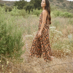 Woman wearing block printed, floral printed Regina corduroy jumpsuit, walking through a field and bushes