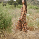 Woman wearing block printed, floral printed Regina corduroy jumpsuit, walking through a field and bushes