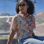Person wearing a floral patterned shirt and sunglasses, sitting in front of an RV