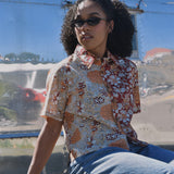Person wearing a floral patterned shirt and sunglasses, sitting in front of an RV