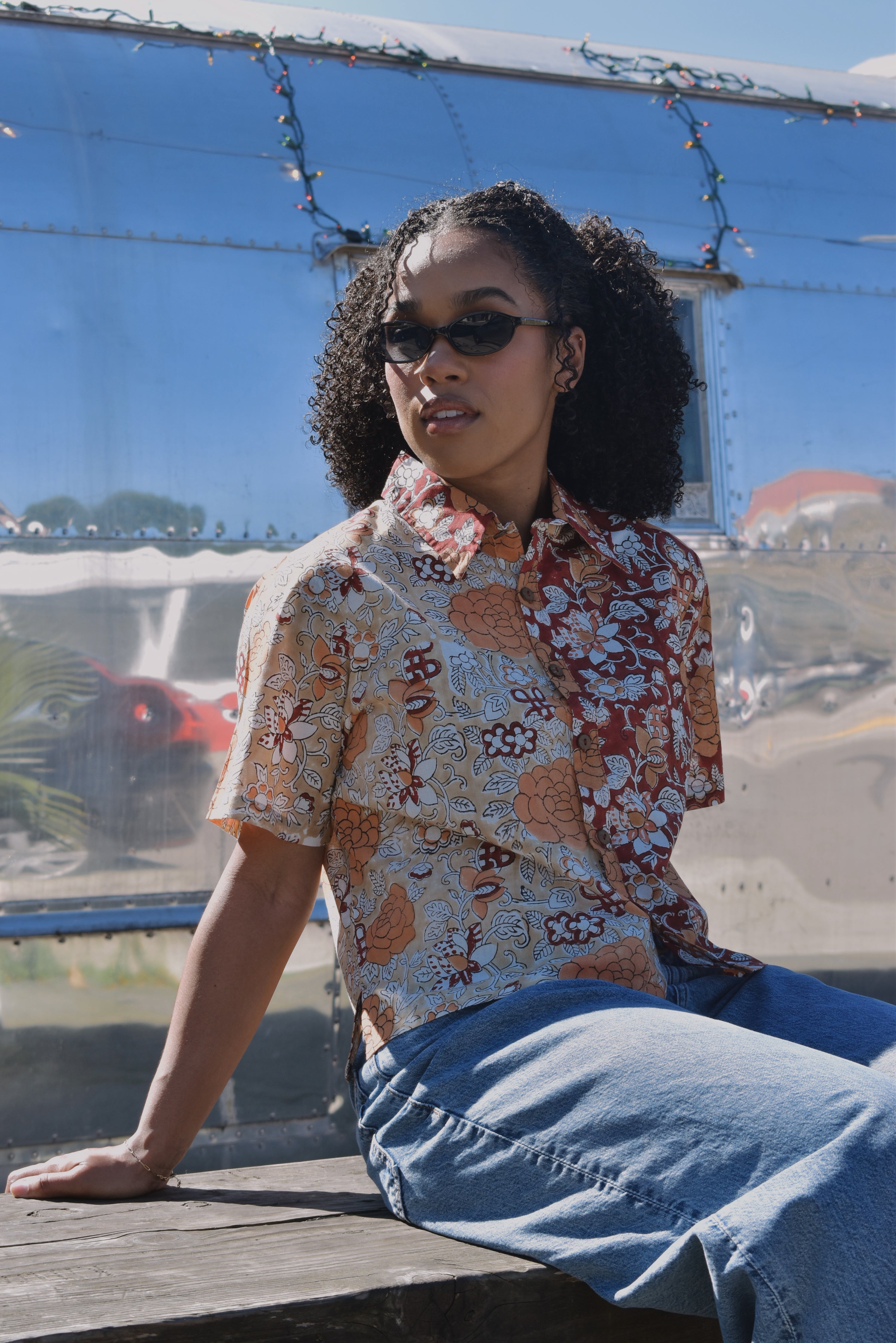 Person wearing a floral patterned shirt and sunglasses, sitting in front of an RV