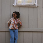 Woman standing outside a building wearing a floral printed shirt and blue jeans with sunglasses