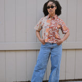 Woman wearing a floral shirt and blue jeans standing in front of a tan building