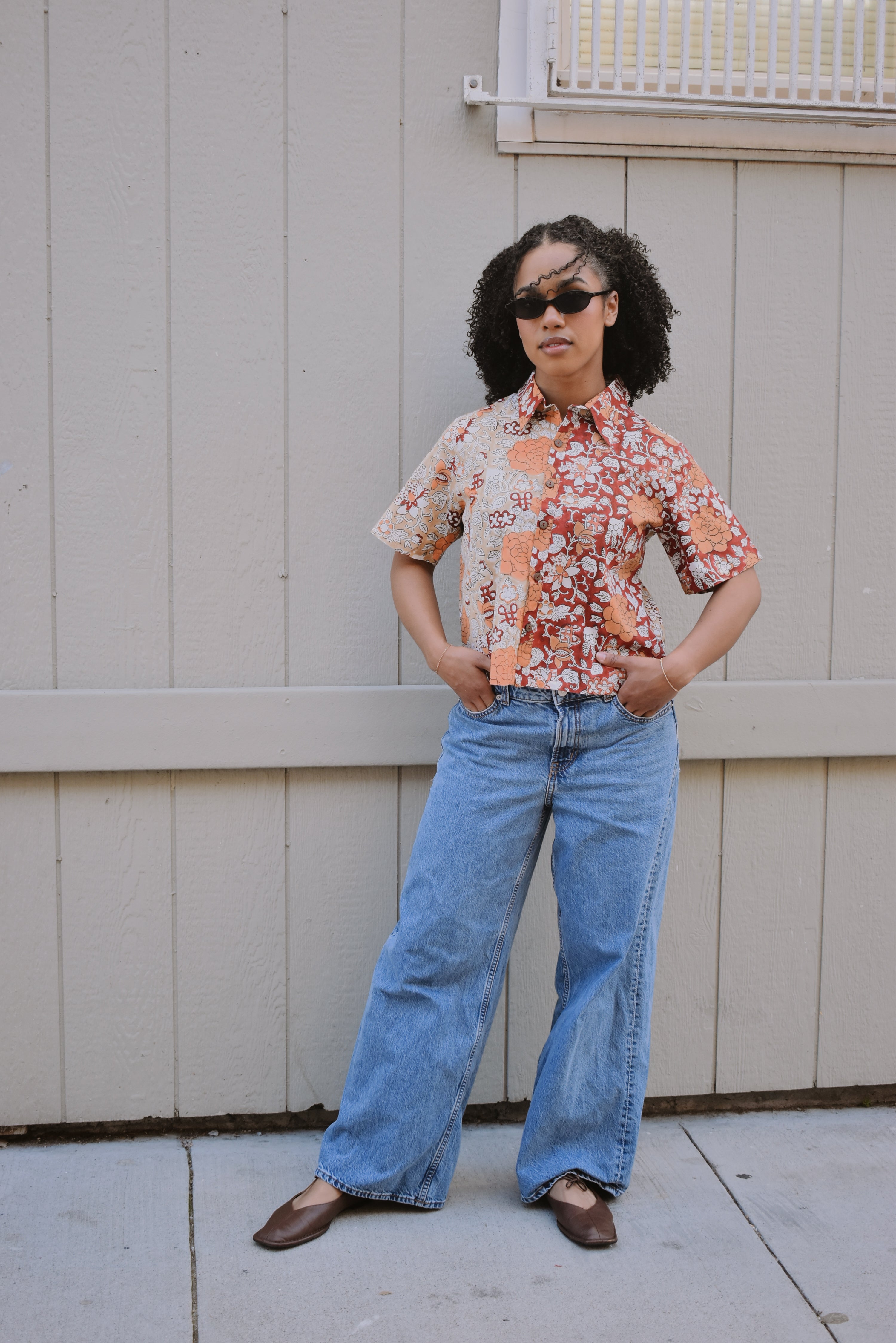 Woman wearing a floral shirt and blue jeans standing in front of a tan building